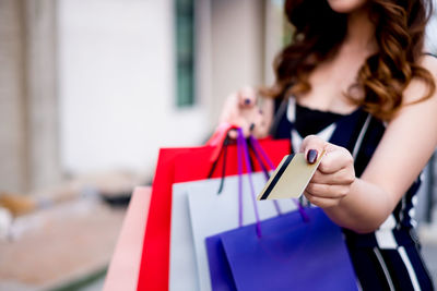Midsection of woman holding shopping bags and credit card in city