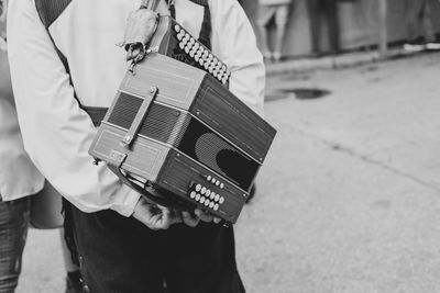 Midsection of man carrying accordion while standing on road