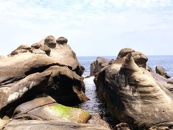 Rock formation on sea shore against sky