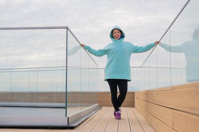 Portrait of smiling woman standing by glass against sky