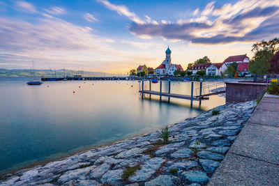 Scenic view of river by building against sky during sunset