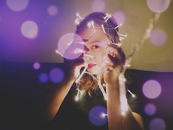 Close-up portrait of young woman holding illuminated lights