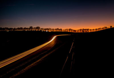 Light trails on highway in city against sky at night