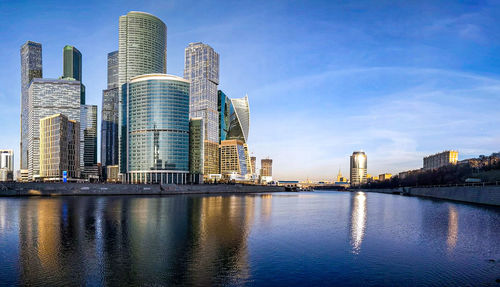 Modern buildings by river against sky in city