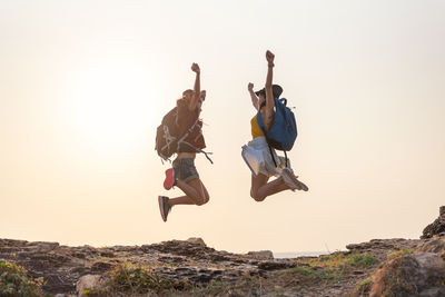 Low angle view of people jumping on rock against sky