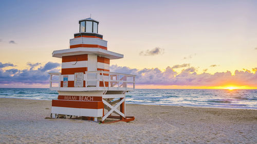 Lighthouse by sea against sky during sunset