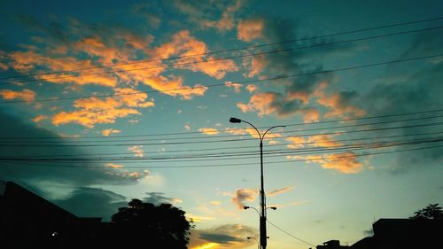 Low angle view of electricity pylon against cloudy sky