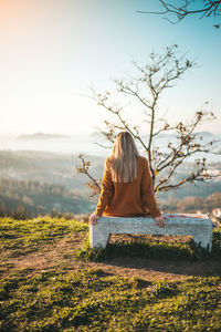Rear view of woman sitting on bench against sky