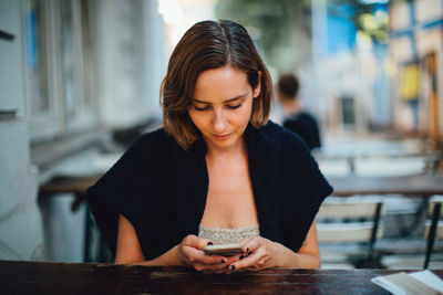 Woman using phone while sitting at outdoor cafe