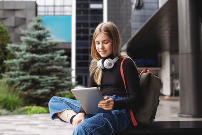 Beautiful fashionable schoolgirl studying online with tablet and headphones sitting on the steps