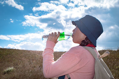 Woman drinking water while standing on land against sky