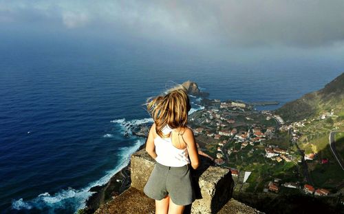 Rear view of woman standing by sea against sky