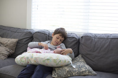 Brother playing with baby girl while sitting on sofa at home