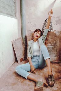 Full length portrait of woman sitting against wall