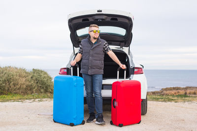 Man standing by car on road against sky