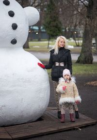 Mother and daughter standing by snowman
