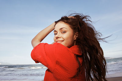 Portrait of smiling young woman standing at beach against sky