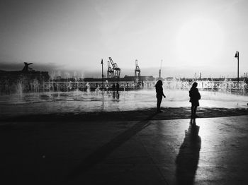 Silhouette women standing by fountain against sky