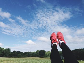 Low section of woman with feet up on field against sky