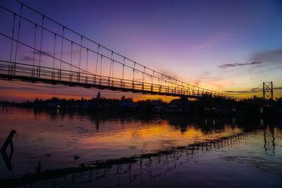 Reflection of bridge on water against orange sky