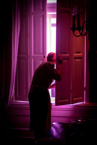 Side view of woman standing against window at home