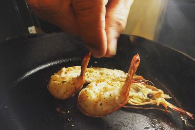 Close-up of person preparing food, sprinkling spices on cooked shrimp on the cooking pan