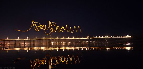 Illuminated text by lake against sky at night
