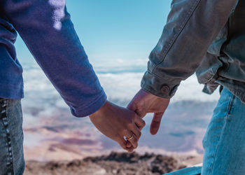 Midsection of man holding hands by sea against sky