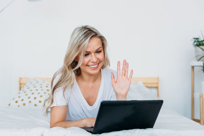 Smiling woman using laptop lying on bed at home