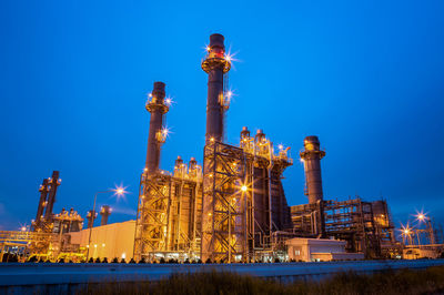 Low angle view of illuminated factory against sky at night