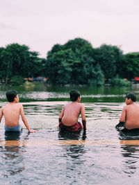 Rear view of boys sitting by lake