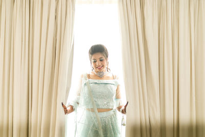 Portrait of a smiling young woman standing against window