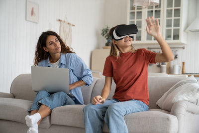 Smiling friends using laptop while sitting on sofa at home