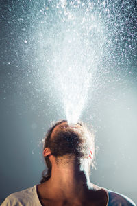 Close-up of bearded young man spraying water against wall