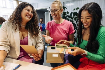 Smiling businesswoman discussing with female colleagues holding box at office