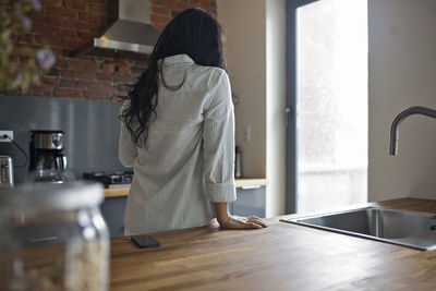 Rear view of woman standing in kitchen at home