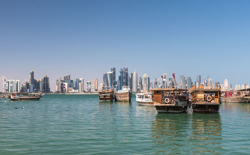 Boats moored in river with city in background