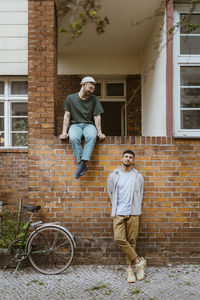 Man looking at boyfriend leaning on brick wall by bicycle outside house