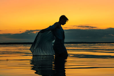 Silhouette woman standing in sea against sky during sunset