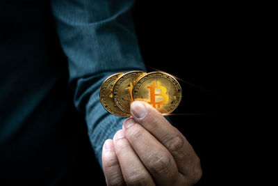 Close-up of hand holding coin against black background