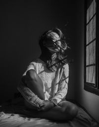 Young woman sitting on bed at home