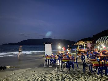 Chairs and tables on beach against sky at night