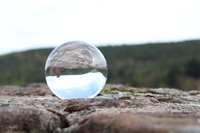 Close-up of crystal ball on field against sky