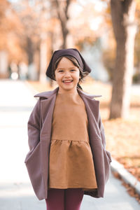 Happy smiling child 4-5 year old wear jacket and hat in park with fall leaves over nature background