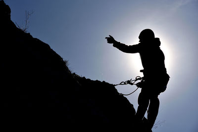 Low angle view of silhouette rock climber on mountain against sky