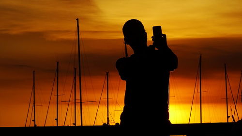 Silhouette man photographing against sky during sunset