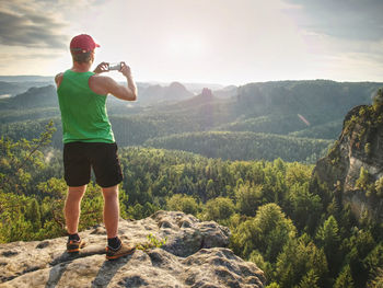 Mobile phone photographer. tourist on the rocky edge take phone pictures. man is taking nature pictu