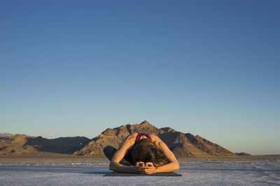 Woman exercising while sitting on mat against clear blue sky during sunset