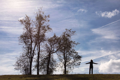 Woman standing by tree on field against sky