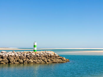 Lighthouse by sea against clear blue sky